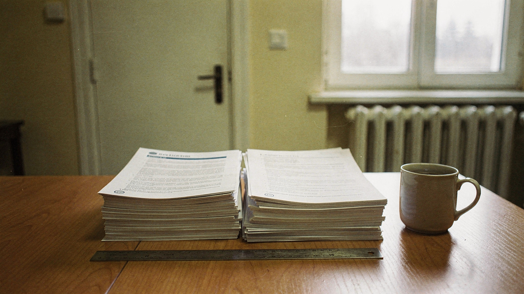 Two stacks of evaluation reports side by side on a plain table with a ruler between them