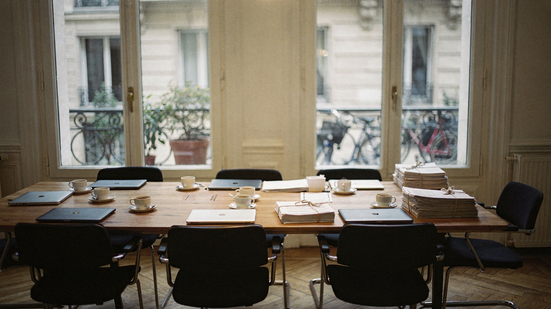 A documentary photograph of a Paris startup office in the morning, founders table with laptops and espresso cups, tall French windows open to a courtyard